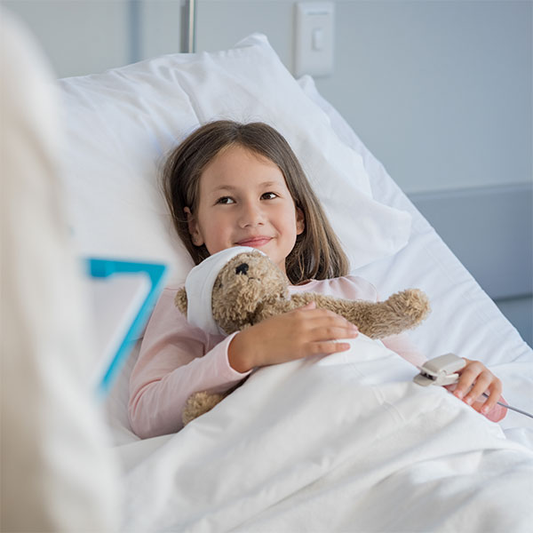 Ein lächelndes Mädchen im Krankenhausbett und einem Teddy im Arm
