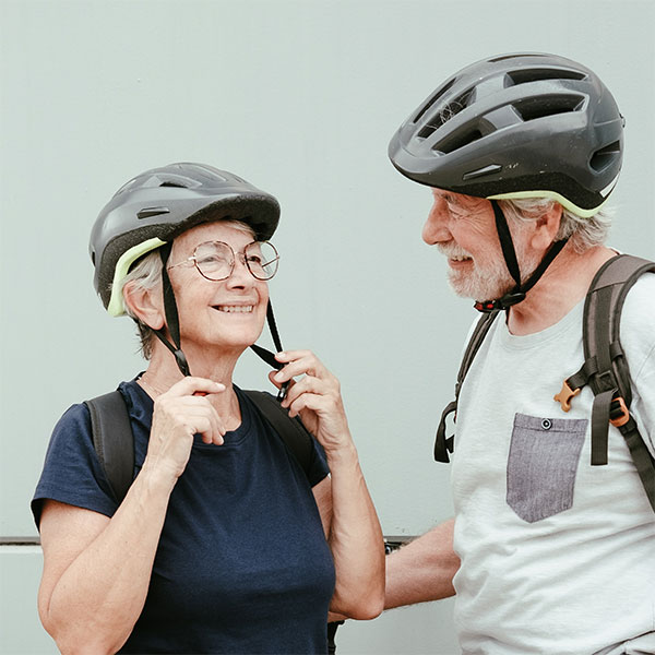 Eine lachende Seniorin und ein lachender Senior. Beide tragen Fahrradhelme.